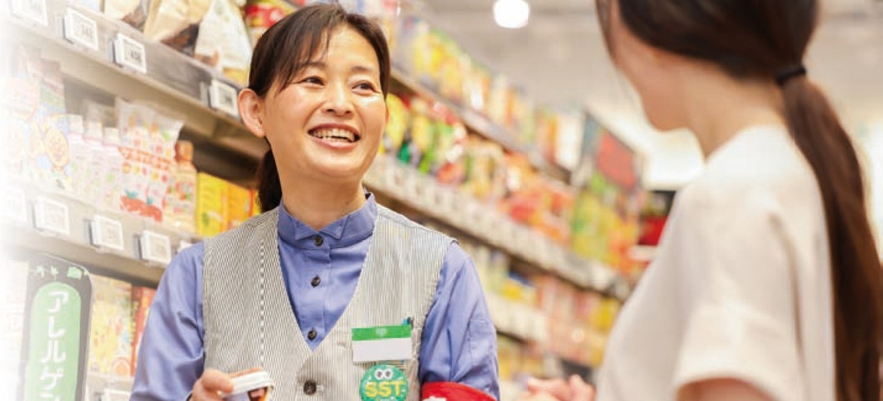 陳列棚の前で来店客と言葉を交わす「案内係」の店員の写真